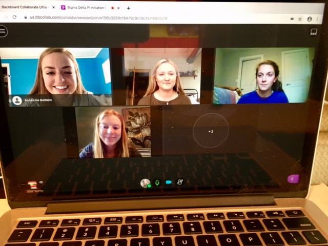 Four Spanish students are visible on a computer screen during a virtual induction ceremony.